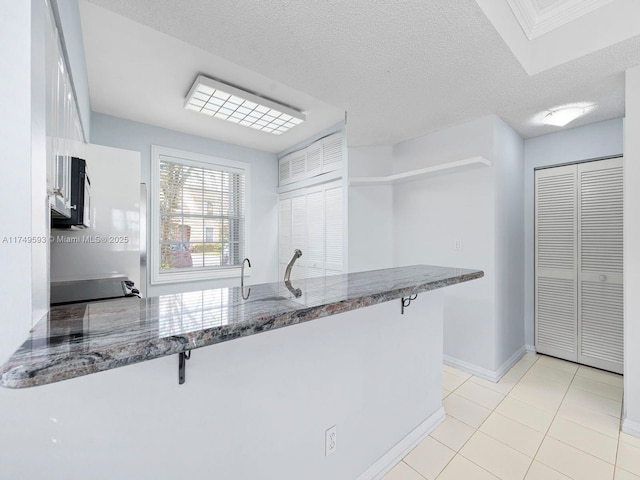 kitchen with a peninsula, a textured ceiling, range, and dark stone countertops