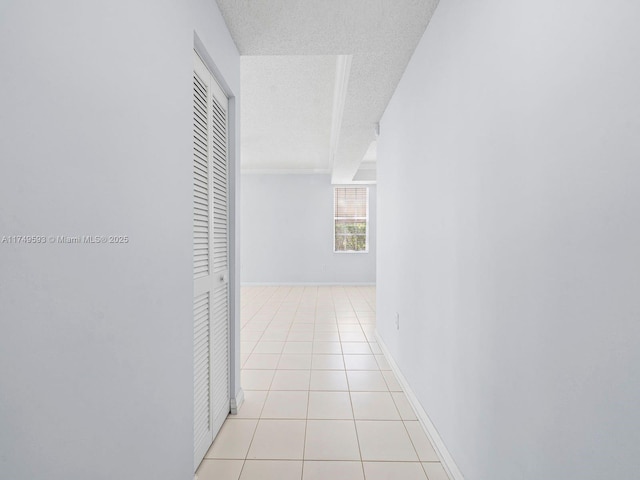 hall featuring light tile patterned flooring, a textured ceiling, and baseboards