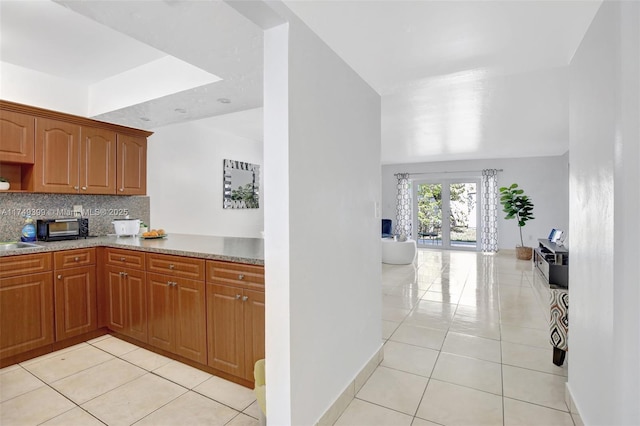 kitchen featuring light tile patterned floors, baseboards, brown cabinetry, and backsplash