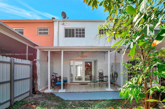 rear view of property featuring french doors, a patio area, fence, and stucco siding