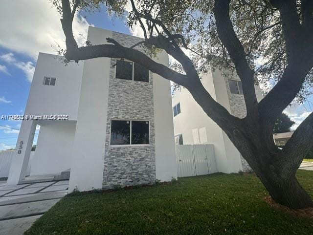 view of side of property featuring fence, a lawn, stone siding, and stucco siding