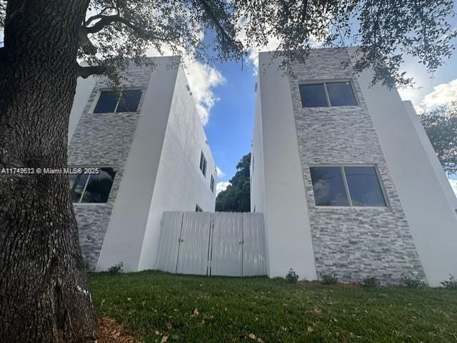 view of side of home featuring a yard, stone siding, and stucco siding