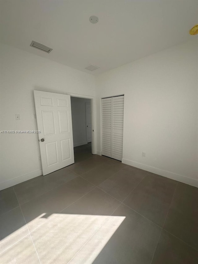 unfurnished bedroom featuring tile patterned flooring, visible vents, a closet, and baseboards