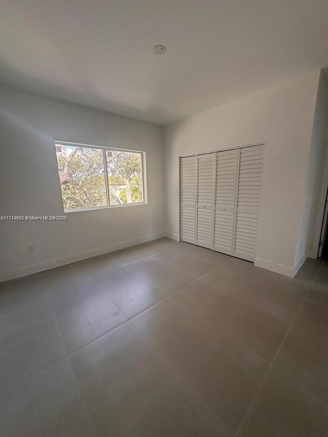 unfurnished bedroom featuring concrete floors, baseboards, and a closet