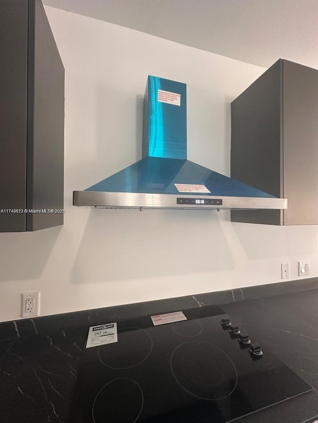 interior details with wall chimney range hood and black electric stovetop