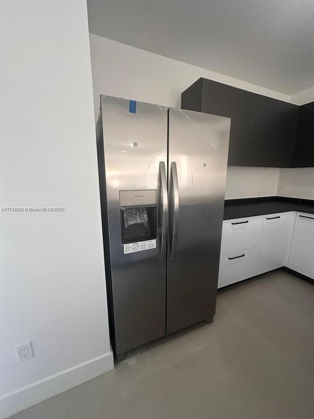 kitchen with baseboards, stainless steel fridge with ice dispenser, white cabinetry, dark countertops, and modern cabinets