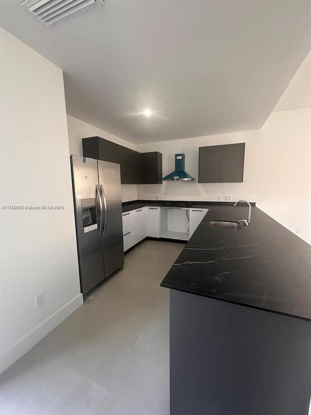 kitchen with a sink, dark countertops, wall chimney exhaust hood, stainless steel fridge with ice dispenser, and baseboards