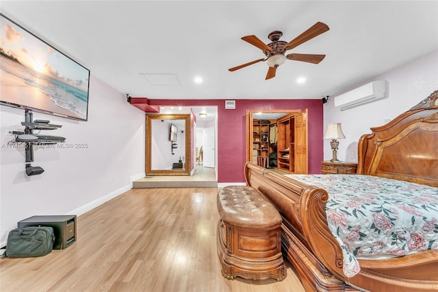 bedroom featuring ceiling fan, light wood-style flooring, baseboards, an AC wall unit, and a spacious closet