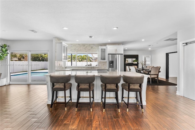 kitchen featuring a breakfast bar, white cabinets, backsplash, stainless steel fridge, and glass insert cabinets