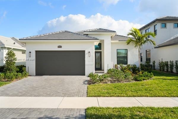 view of front facade featuring stucco siding, a tile roof, decorative driveway, a front yard, and a garage