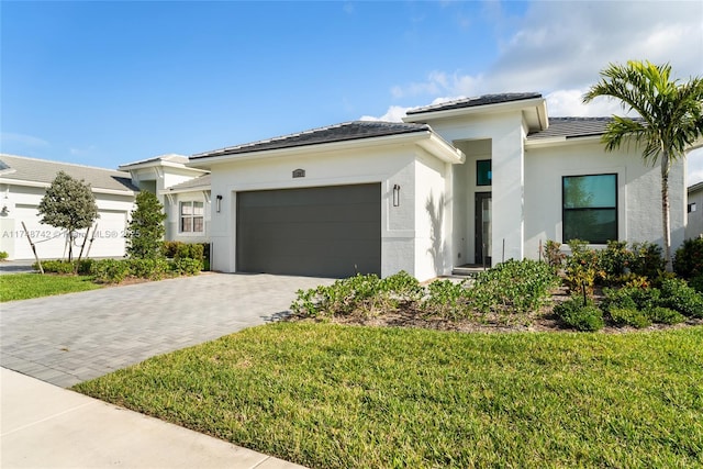 prairie-style house with stucco siding, an attached garage, decorative driveway, and a front lawn