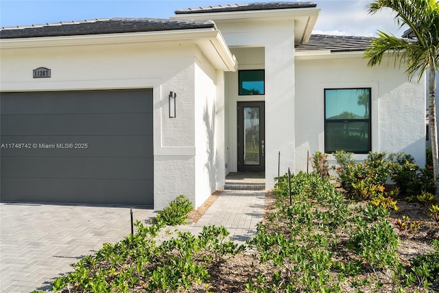 view of exterior entry with decorative driveway, a tile roof, an attached garage, and stucco siding