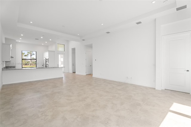 unfurnished living room featuring visible vents, recessed lighting, a tray ceiling, and a sink
