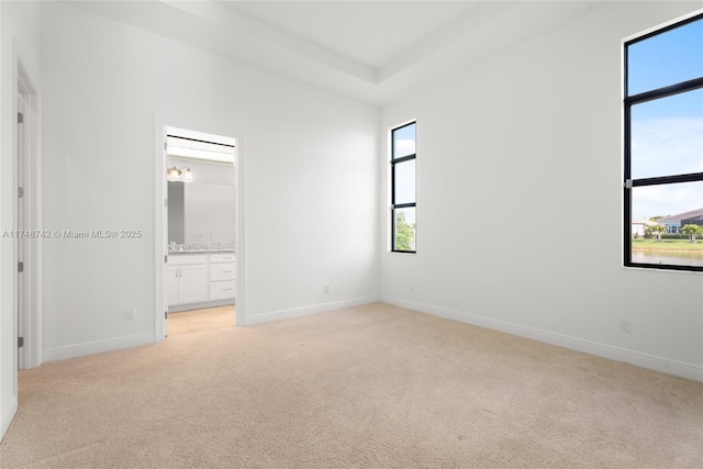 unfurnished bedroom with ensuite bath, light colored carpet, baseboards, and a raised ceiling