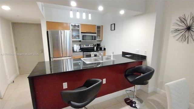 kitchen featuring dark countertops, a kitchen bar, appliances with stainless steel finishes, and glass insert cabinets