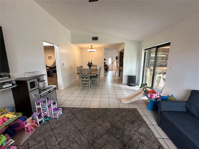 living area featuring light tile patterned floors, lofted ceiling, visible vents, a textured ceiling, and baseboards