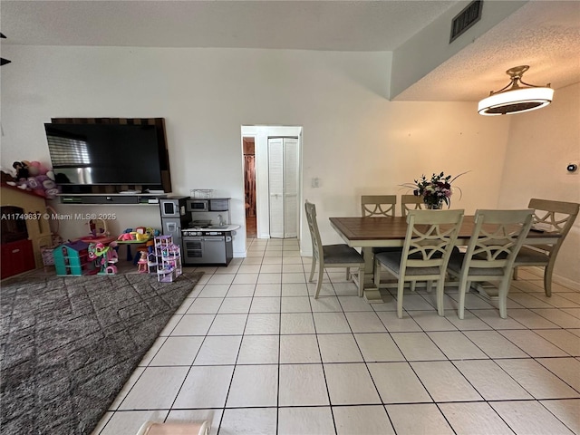 dining area featuring a textured ceiling, light tile patterned flooring, visible vents, and baseboards