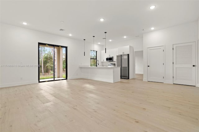 unfurnished living room with light wood finished floors, baseboards, visible vents, a sink, and recessed lighting