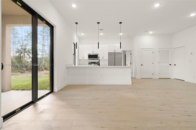 kitchen featuring light wood finished floors, hanging light fixtures, stainless steel appliances, light countertops, and white cabinetry