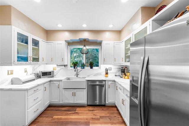 kitchen featuring stainless steel appliances, a sink, white cabinetry, glass insert cabinets, and pendant lighting