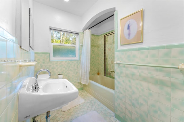 bathroom with a wainscoted wall, a sink, tile walls, tile patterned floors, and shower / tub combo with curtain
