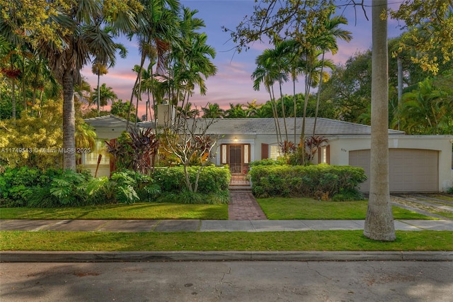 view of front facade featuring an attached garage, a tile roof, driveway, stucco siding, and a front lawn