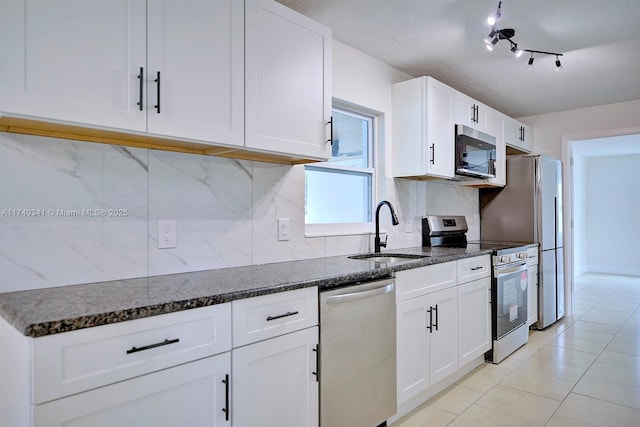 kitchen featuring white cabinets, dark stone countertops, a sink, stainless steel appliances, and backsplash