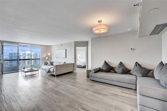 living area with a view of city, a wall of windows, light wood-type flooring, and visible vents