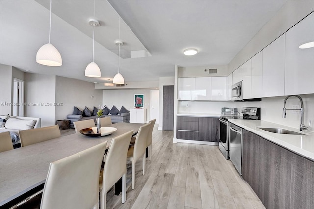 kitchen featuring modern cabinets, appliances with stainless steel finishes, open floor plan, pendant lighting, and a sink