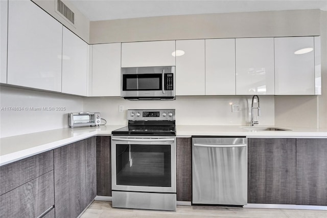 kitchen with modern cabinets, appliances with stainless steel finishes, white cabinets, and a sink