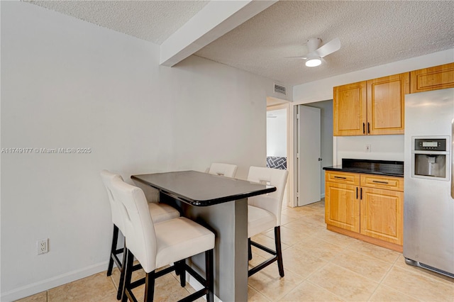 kitchen featuring ceiling fan, a textured ceiling, visible vents, stainless steel fridge with ice dispenser, and dark countertops