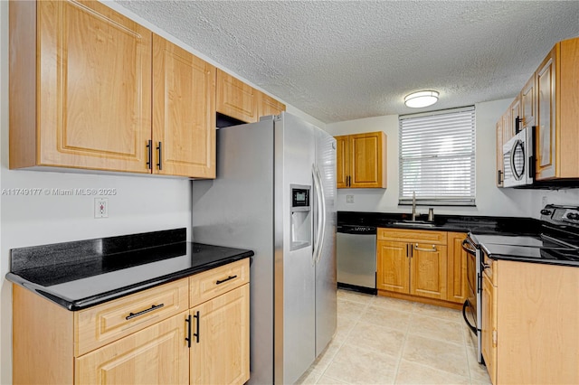 kitchen with light tile patterned floors, a textured ceiling, a sink, appliances with stainless steel finishes, and dark countertops