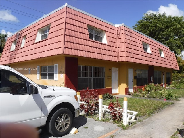 view of front of property with stucco siding, a tiled roof, and mansard roof