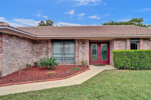 entrance to property featuring french doors, brick siding, a lawn, and a tiled roof