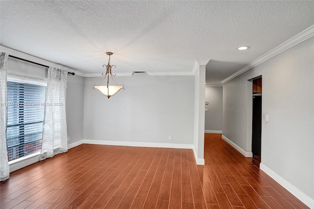 spare room with a textured ceiling, wood finished floors, baseboards, and ornamental molding