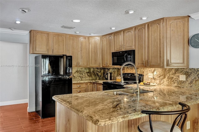 kitchen featuring light stone counters, dark wood finished floors, a peninsula, decorative backsplash, and black appliances