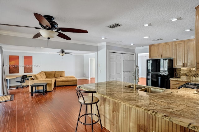 kitchen featuring visible vents, a sink, freestanding refrigerator, a peninsula, and light stone countertops