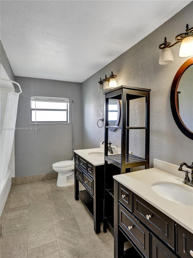 full bathroom featuring toilet, two vanities, a sink, a textured ceiling, and a textured wall