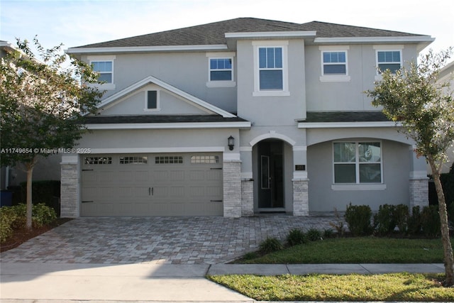 view of front of property featuring decorative driveway, roof with shingles, an attached garage, and stucco siding