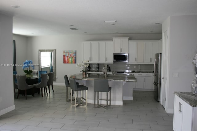 kitchen with appliances with stainless steel finishes, a sink, a breakfast bar, and white cabinets