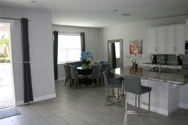 kitchen with visible vents, white cabinetry, a sink, dark stone counters, and a kitchen bar