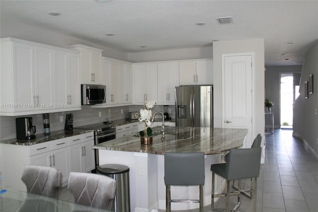 kitchen featuring white cabinetry, a large island, dark stone counters, and stainless steel appliances