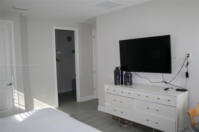 bedroom featuring visible vents, a spacious closet, baseboards, and wood finished floors