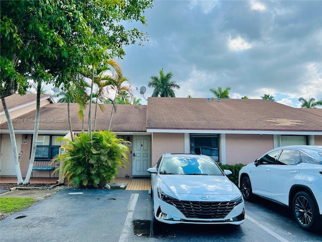 view of front facade with a shingled roof, uncovered parking, and stucco siding