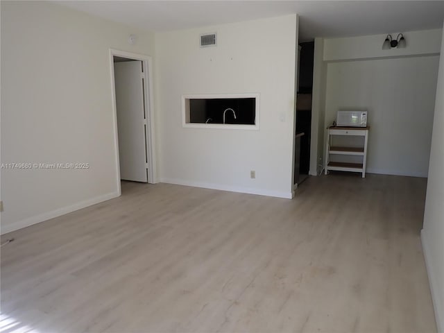 empty room featuring light wood-style flooring, visible vents, and baseboards