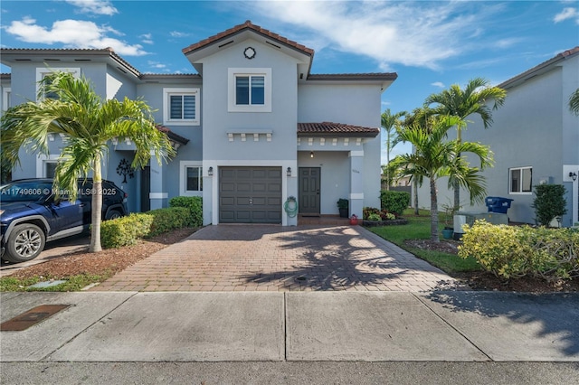 mediterranean / spanish-style home featuring a garage, decorative driveway, a tile roof, and stucco siding