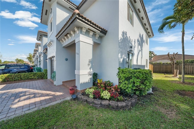 view of home's exterior with a tile roof, fence, a lawn, and stucco siding