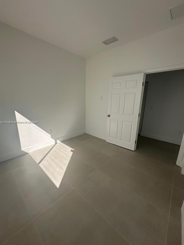 unfurnished room with visible vents, dark tile patterned floors, and baseboards