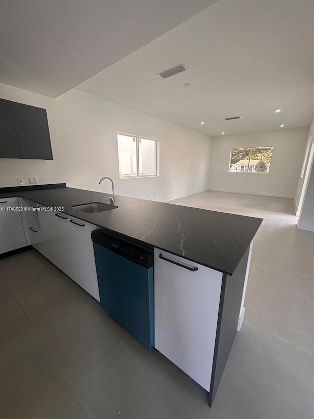 kitchen with dark countertops, dishwashing machine, visible vents, and a sink