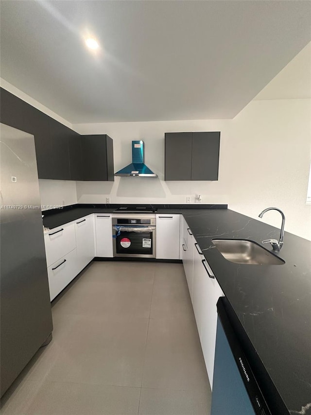 kitchen with wall chimney range hood, modern cabinets, appliances with stainless steel finishes, and a sink